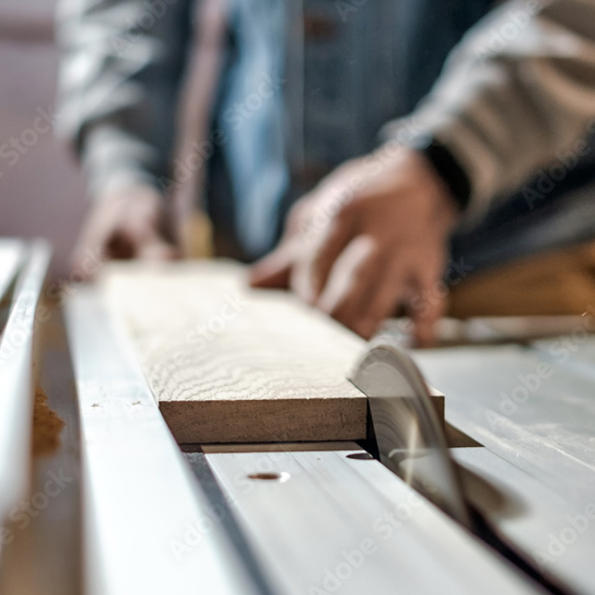 Person using a table saw to cut wood, focus on the blade and wood plank in a workshop setting.