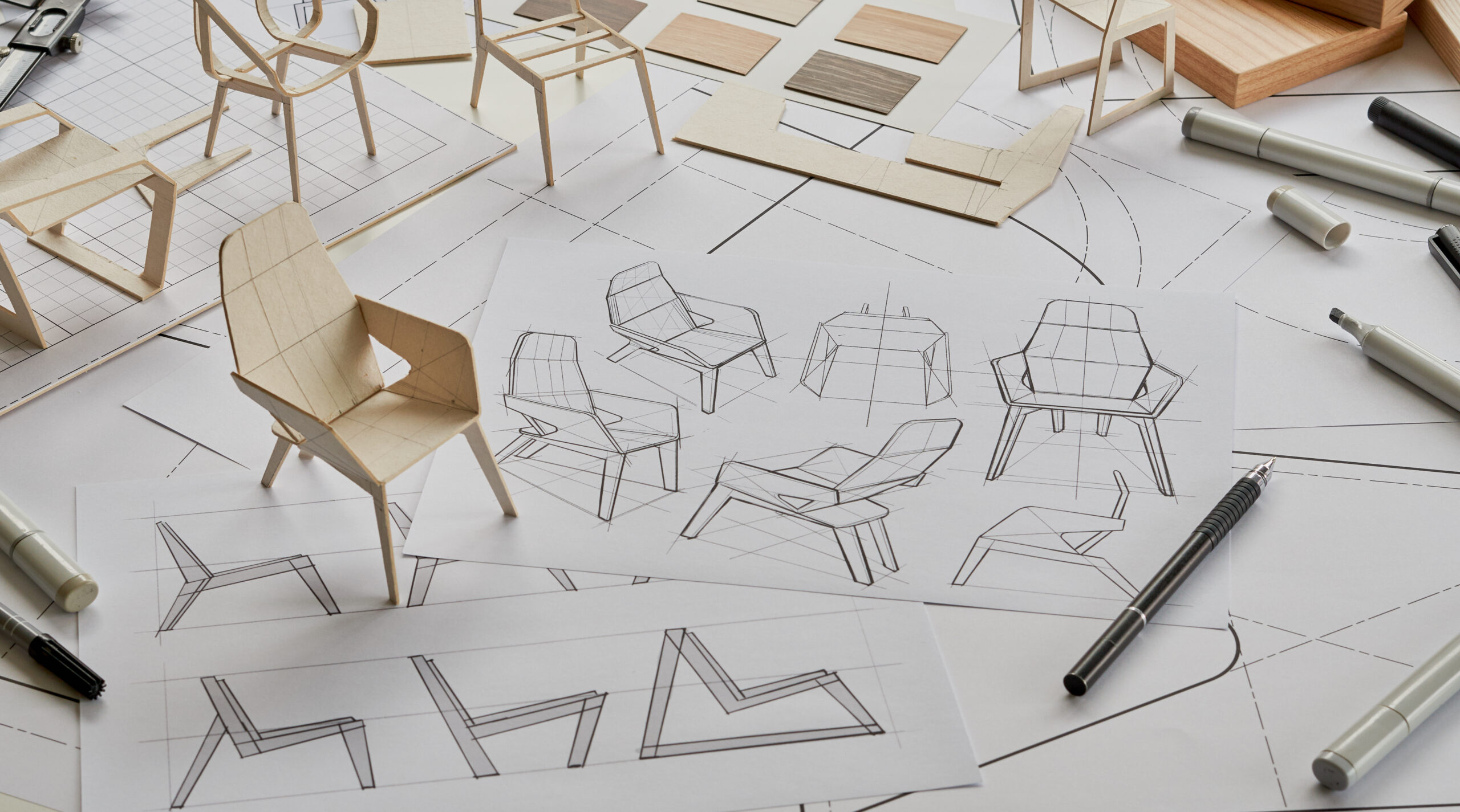 Chair design sketches with miniature models and drafting tools on a workspace.