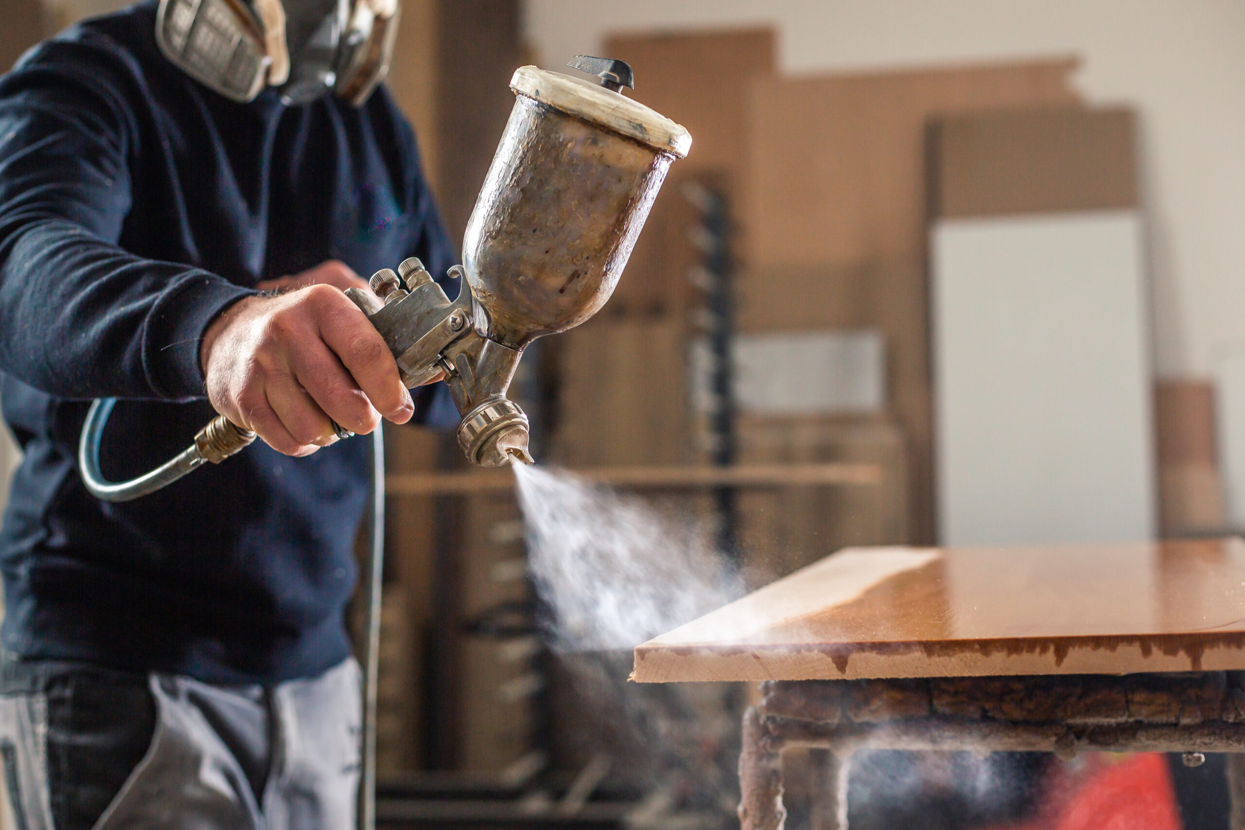 Person using a spray gun to apply finish on wooden furniture in workshop.