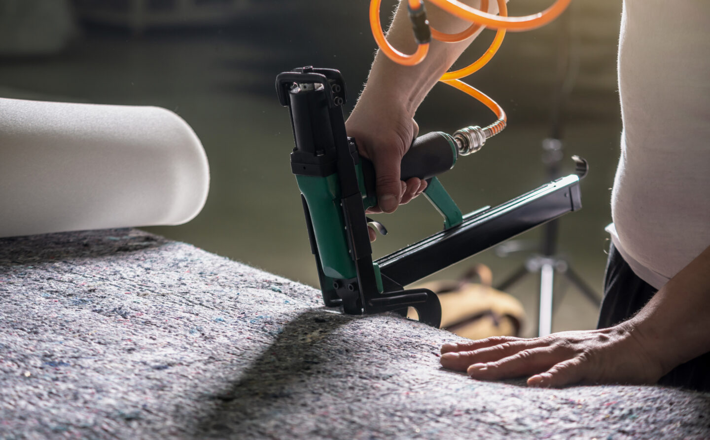 Person using an upholstery stapler on fabric with a foam roll, highlighting professional furniture crafting.