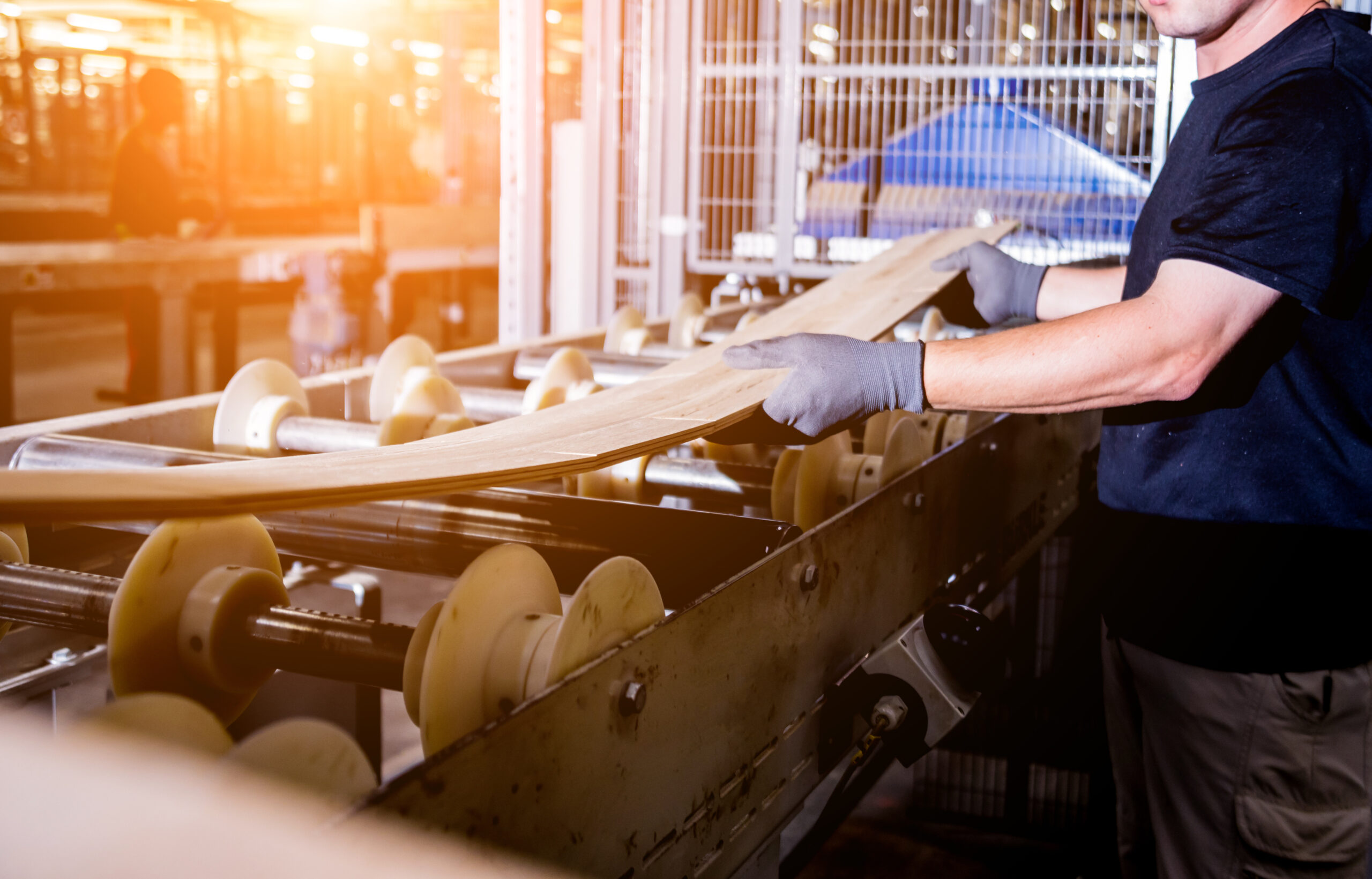 Worker handling wood on conveyor in a bright factory setting.