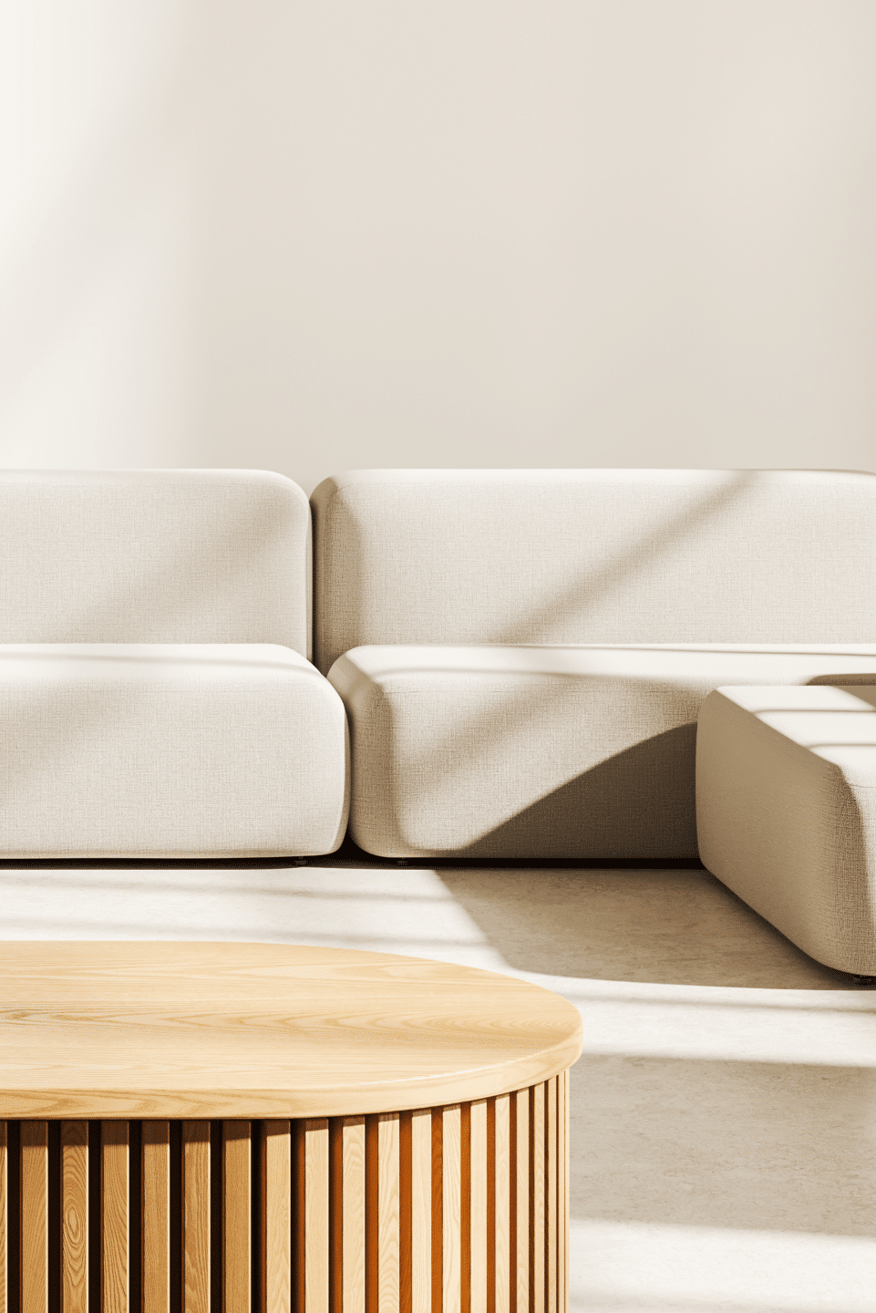 Modern beige sofa and round wooden coffee table in a sunlit minimalist living room.